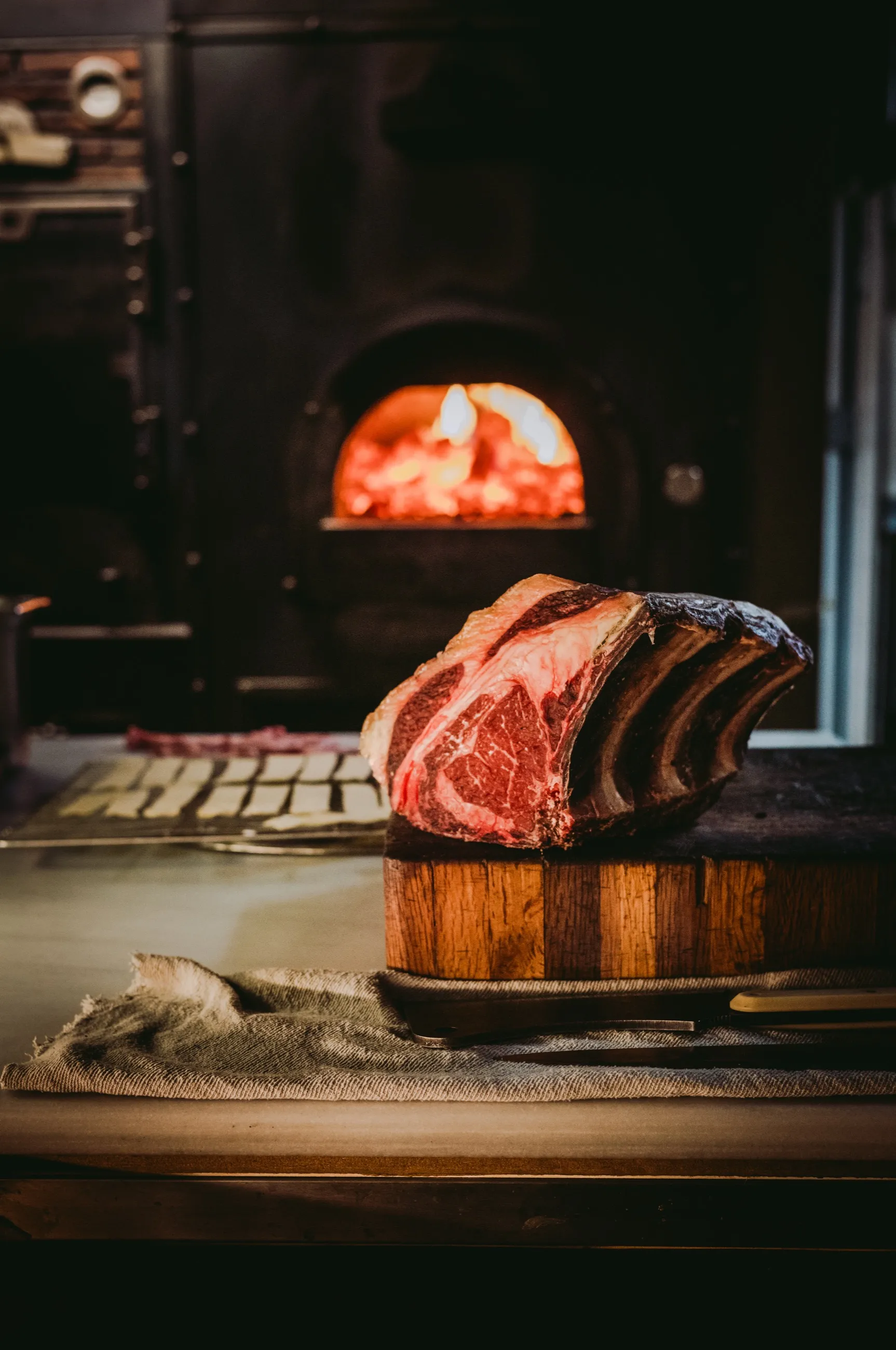 Costilla de vaca sobre una tabla, con el horno de leña encendido al fondo