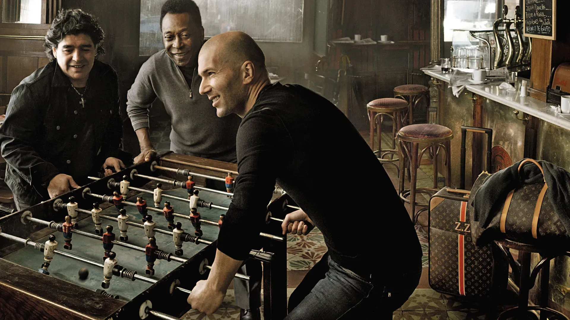Maradona, Pelé and Zidane playing table football in the bar, with the marble counter and tiled floor behind them